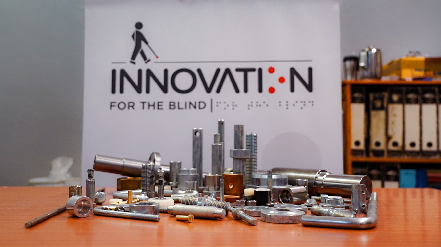 Machined components (pins, bushes and fittings) in front of the Innovation for the Blind banner